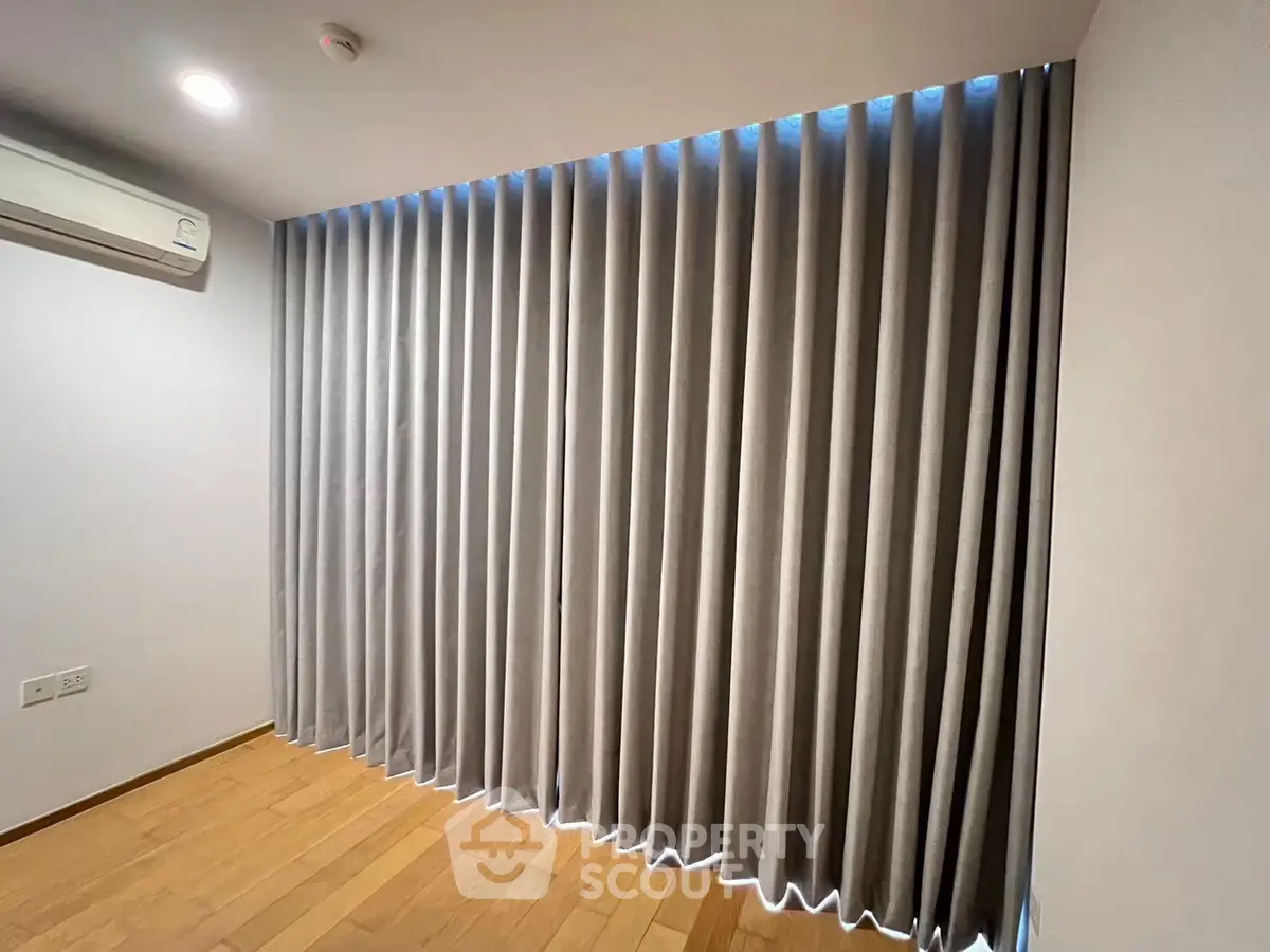Spacious room with elegant floor-to-ceiling curtains and wooden flooring, perfect for modern living.