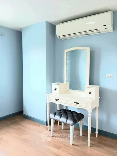 Charming bedroom corner with elegant vanity and plush stool, featuring soothing blue walls and modern air conditioning.
