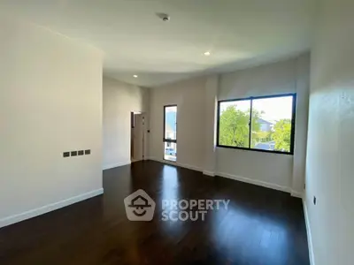 Spacious empty room with dark wood flooring and large windows offering natural light.