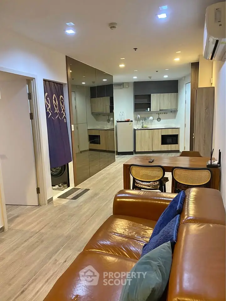 Modern living room with leather sofa, mirrored wall, and open kitchen layout in stylish apartment.
