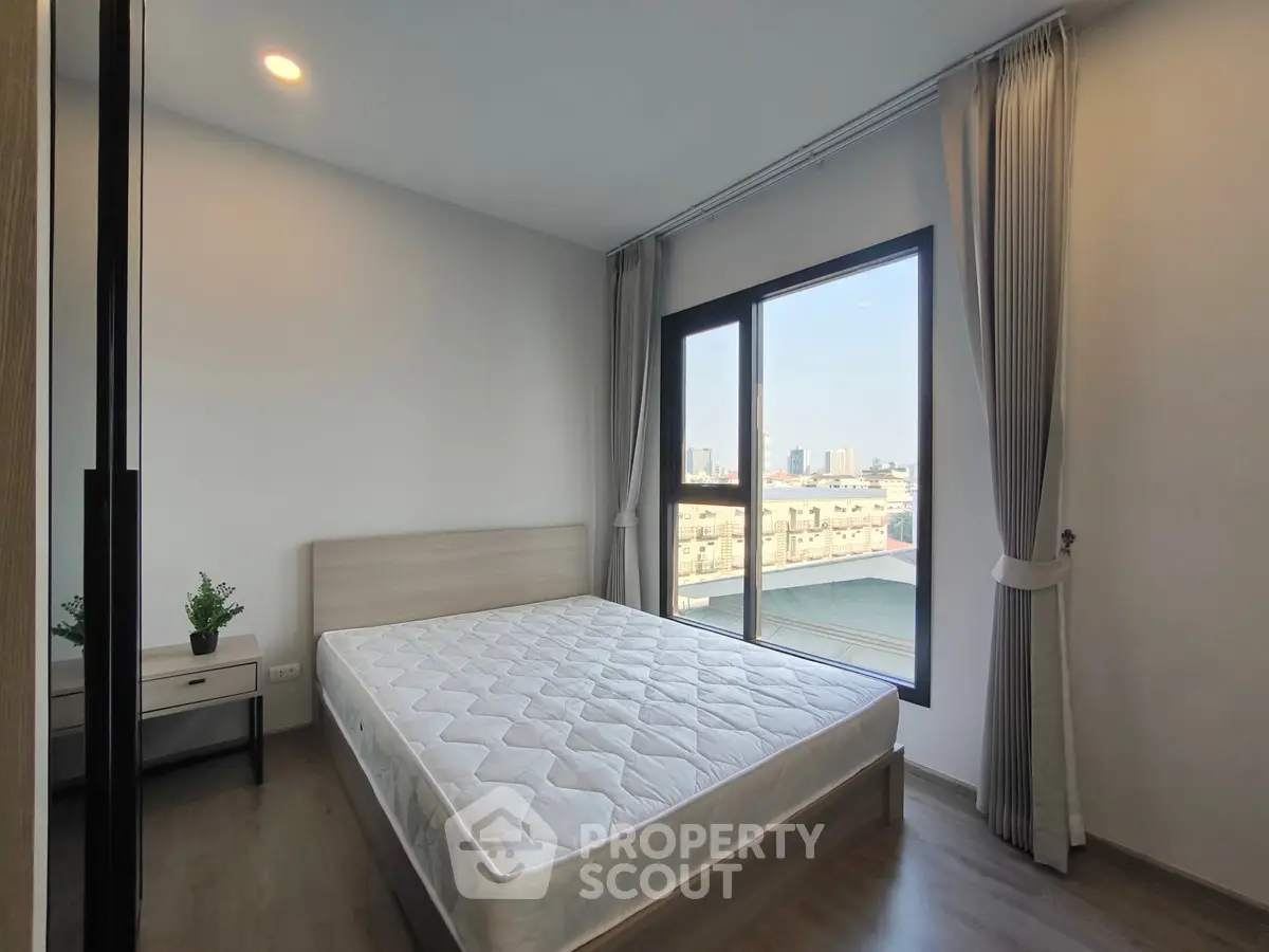 Modern bedroom with large window and city view, featuring a comfortable bed and stylish decor.
