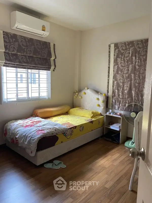 Cozy bedroom with wooden flooring and natural light, featuring a comfortable bed and air conditioning.