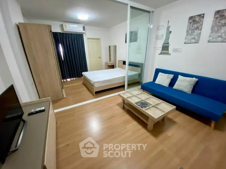 Modern studio apartment with wooden flooring, blue sofa, and sliding glass partition.