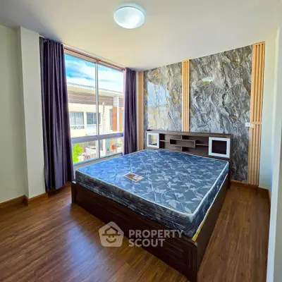 Modern bedroom with large window and stylish accent wall in a bright apartment.