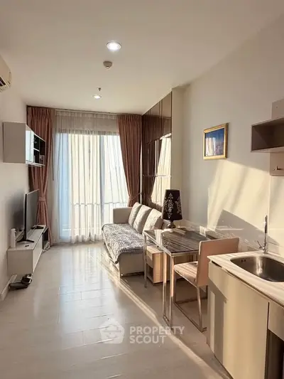 Modern living room with natural light, sleek furniture, and a compact kitchen area, perfect for urban living.