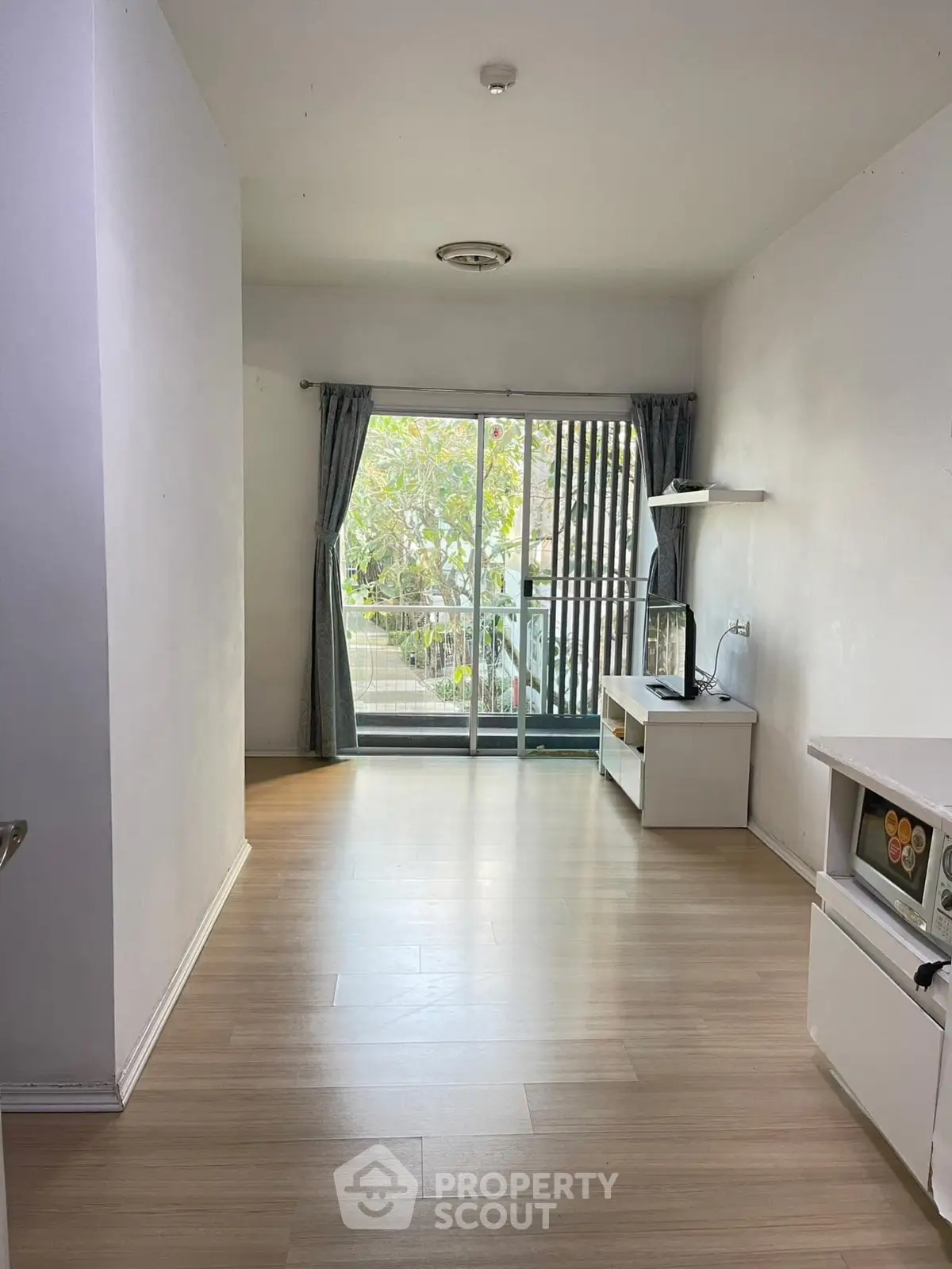 Spacious living room with sliding glass doors leading to a balcony, featuring light wood flooring and natural light.