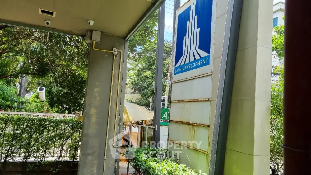 Modern building entrance with lush greenery and development sign