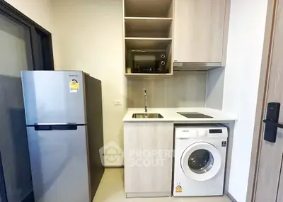 Modern compact kitchen with fridge, washing machine, and microwave in stylish apartment.