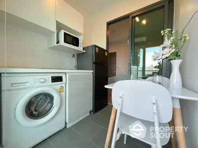 Modern kitchen with washing machine, microwave, and dining area in a compact apartment.