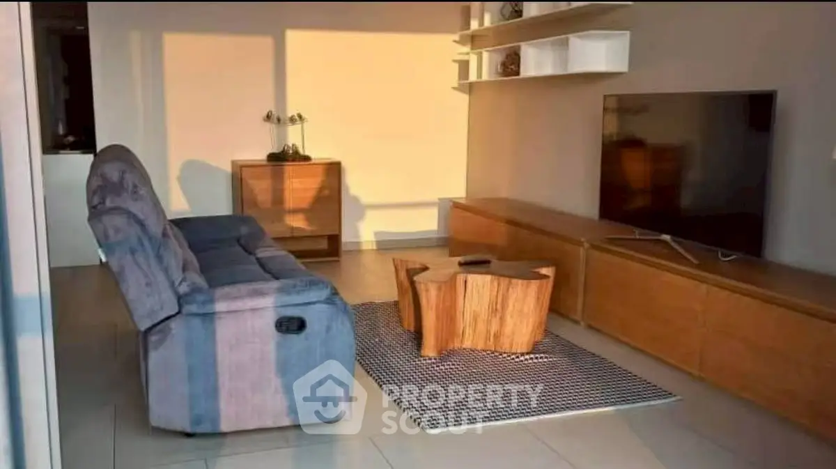 Modern living room with stylish furniture and large TV, bathed in warm sunlight.