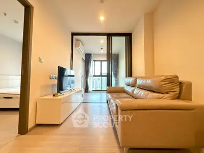 Modern living room with leather sofa and TV, leading to a bright balcony.