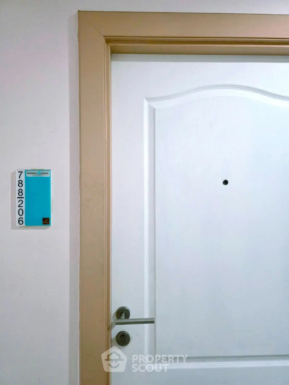 Modern apartment entrance with sleek white door and stylish beige frame, featuring a peephole and room number.