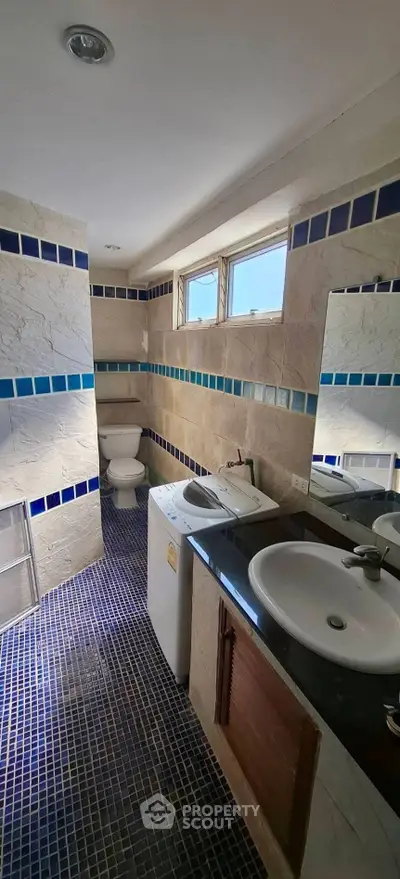Charming bathroom with dual sinks and modern design, featuring blue tile accents and natural light.