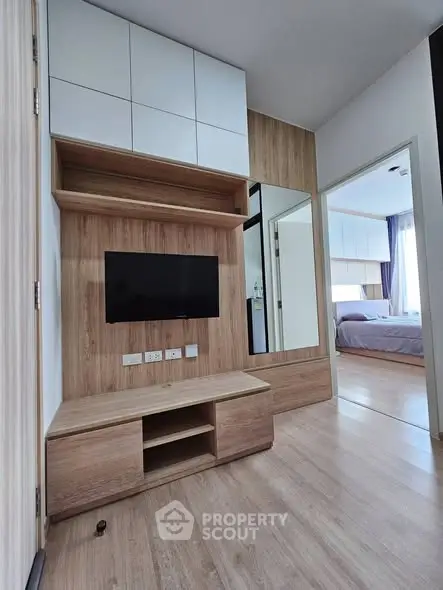 Modern apartment interior with sleek wooden TV unit and view into cozy bedroom.