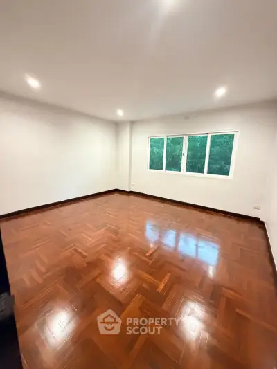 Spacious empty room with polished wooden floors and large window with green view.