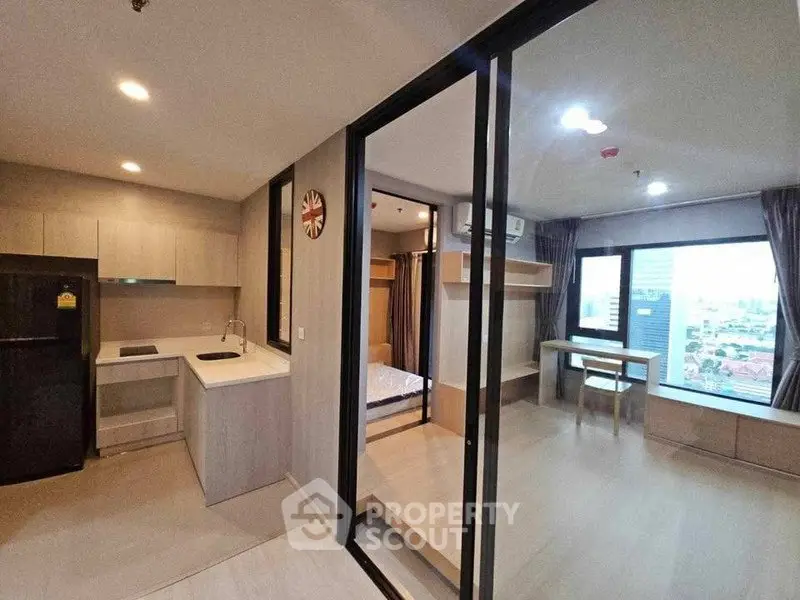 Modern open-layout apartment with kitchen and living area, featuring large windows and city view.