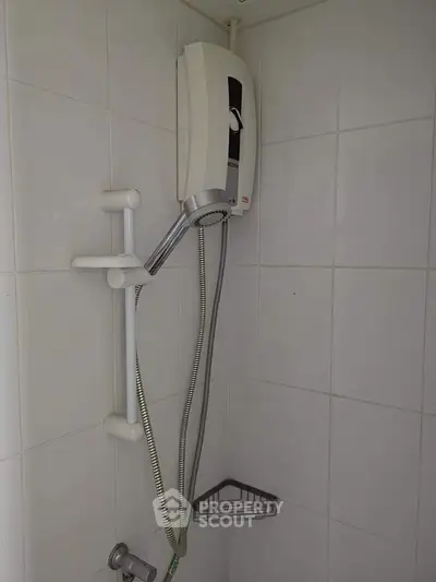 Compact bathroom shower area with water heater and tiled walls.