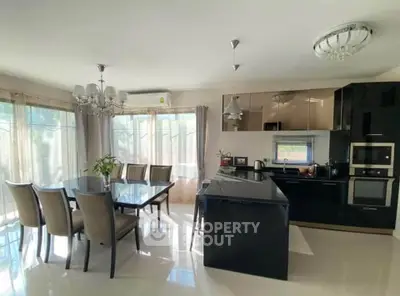 Modern kitchen with sleek black cabinets and elegant dining area, flooded with natural light.