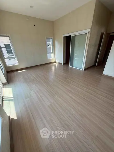Spacious empty room with wooden flooring and large windows, perfect for customization.