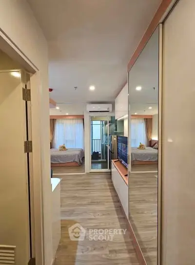 Modern apartment hallway leading to a cozy bedroom with mirrored closet and wooden flooring.