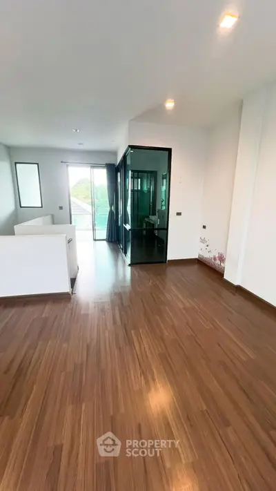 Spacious modern living room with wooden flooring and glass doors leading to balcony.