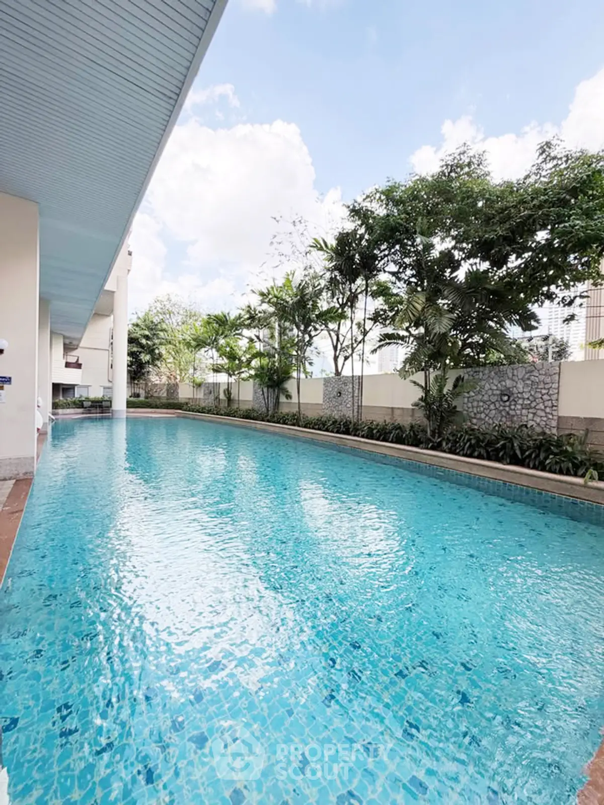 Luxurious outdoor swimming pool with lush greenery and clear blue skies, perfect for relaxation and leisure.