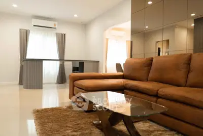 Spacious living room with modern brown leather sofa and glass coffee table, featuring elegant decor and ample natural light.
