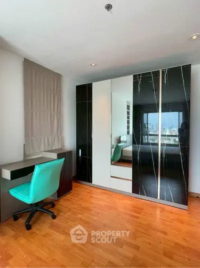 Modern bedroom with stylish wardrobe and city view, featuring a sleek desk and vibrant chair.