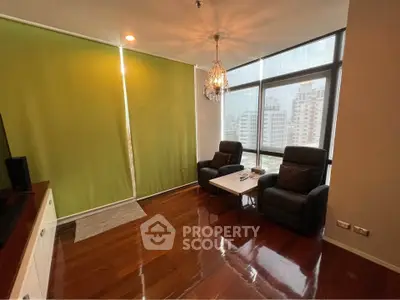 Modern living room with large windows and city view, featuring elegant chandelier and comfortable seating.