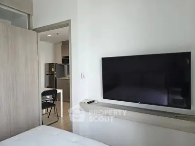 Modern apartment interior with wall-mounted TV and view into sleek kitchen area.