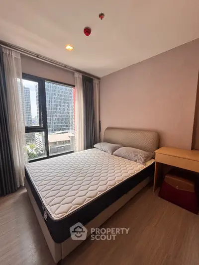 Modern bedroom with large window offering city view, featuring a comfortable bed and stylish decor.