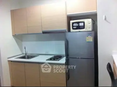 Modern compact kitchen with sleek cabinets, stainless steel fridge, and microwave, perfect for urban living.
