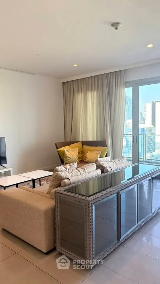 Spacious living room with modern decor and city view, featuring elegant furniture and large windows.