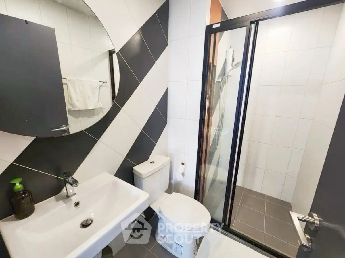 Modern bathroom with sleek design, featuring a round mirror, glass shower enclosure, and stylish tile patterns.