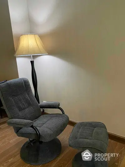 Cozy reading nook with comfortable reclining chair and matching ottoman, complemented by a warm floor lamp, set against a neutral wall on elegant hardwood flooring.