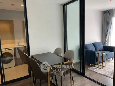 Modern apartment with sleek dining area and cozy living room, featuring glass partition and stylish furniture.