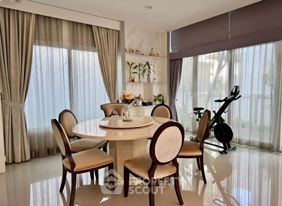 Elegant dining area with round table and exercise bike, featuring large windows and stylish decor.