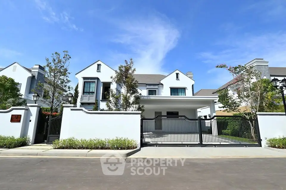 Elegant white two-story house with gated entrance and lush landscaping under a clear blue sky.