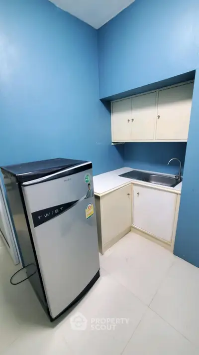 Compact kitchen with blue walls, white cabinets, and a sleek refrigerator.