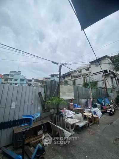 Urban alleyway with residential buildings and outdoor furniture under cloudy sky.