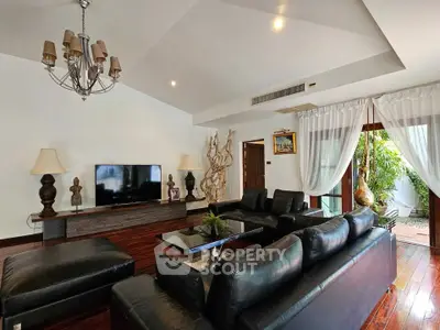 Luxurious living room with elegant decor and garden view, featuring black leather sofas and chandelier.