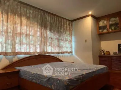 Cozy bedroom with wooden furniture and floral curtains, perfect for relaxation.