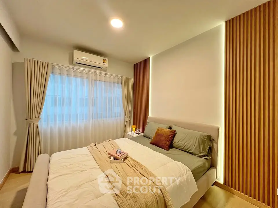 Modern bedroom with stylish wood paneling and cozy bedding in a well-lit apartment.