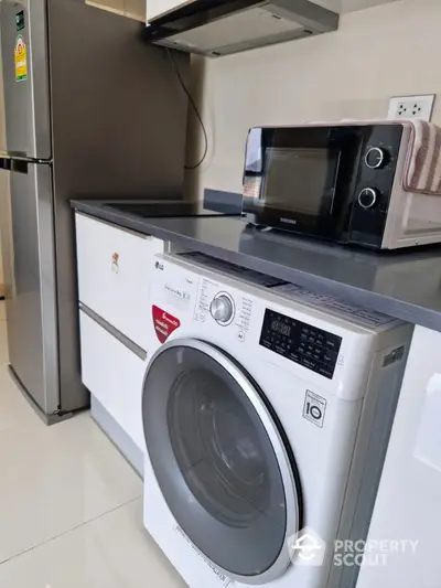 Modern kitchen with washing machine, fridge, and microwave in sleek design.