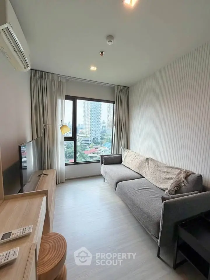 Modern living room with city view, featuring a cozy gray sofa and large window for natural light.