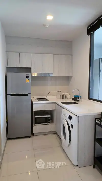 Modern kitchen with sleek appliances including fridge, washing machine, and microwave in a compact layout.