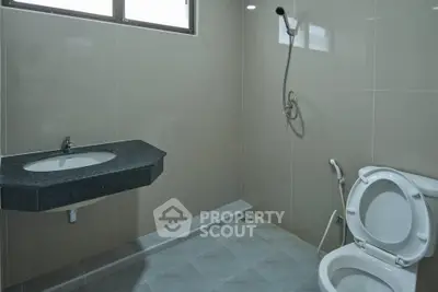 Modern bathroom with sleek fixtures and neutral tiles, featuring a wall-mounted sink and shower.