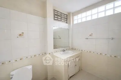 Spacious bathroom with tiled walls and a large mirror, featuring a modern sink and ample natural light.