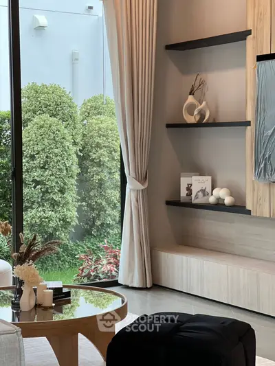 Elegant living room with modern decor and garden view, featuring stylish shelves and a glass coffee table.