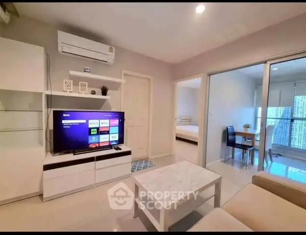 Modern living room with sleek furniture and smart TV, open view to dining area and bedroom.